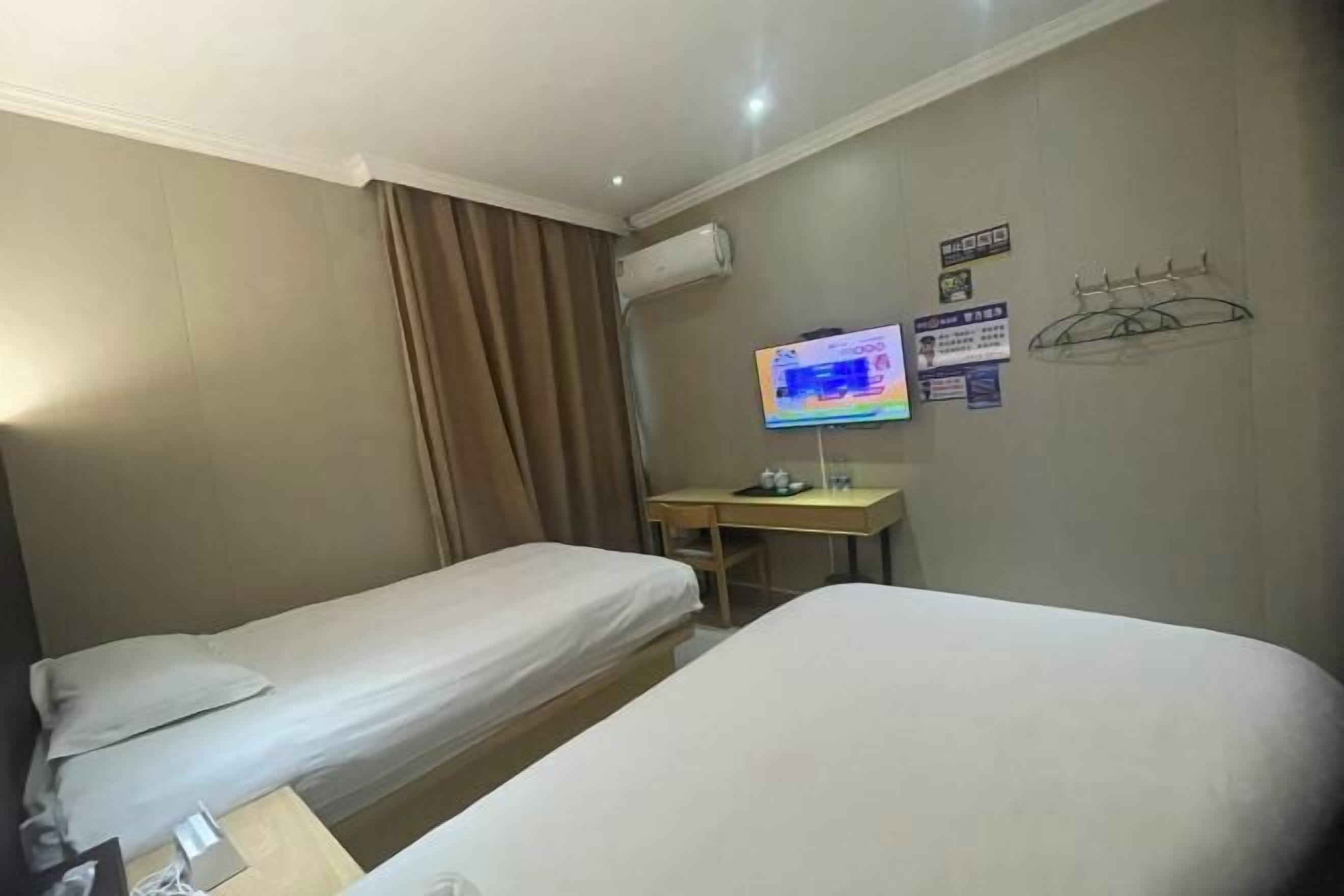 Et hotelværelse med to senge, et skrivebord med en computer, aircondition og et fjernsyn på væggen.