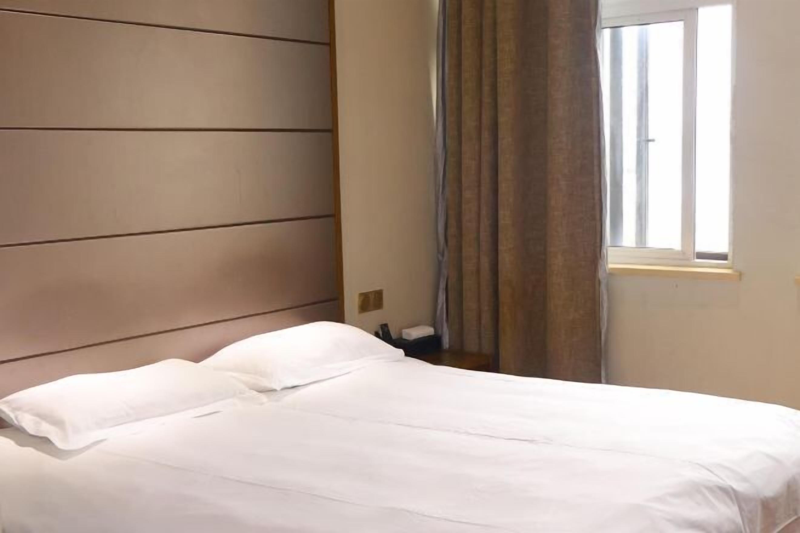 Un letto rifatto con lenzuola bianche in una stanza con testiera in legno e finestra con tende.