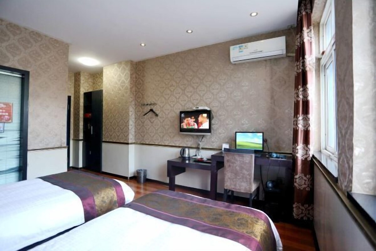 Ein Hotelzimmer mit zwei Betten, einem Schreibtisch mit Computer, einer Klimaanlage und einem Fernseher an der Wand.