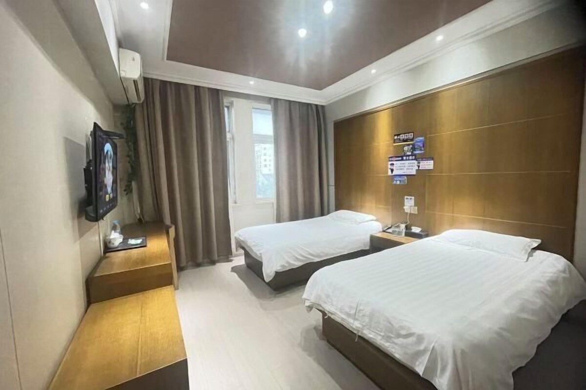 Ein Hotelzimmer mit zwei Betten, einem Fernseher, einem Schreibtisch und einem Fenster mit Vorhängen.