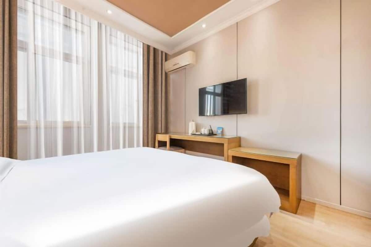 Ein Hotelzimmer mit einem großen Bett, einem Holztisch, einem flachbildfernseher an der Wand und einer Klimaanlage.