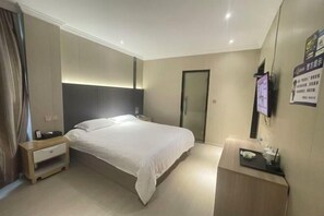 Ein Hotelzimmer mit Bett, Nachttisch und Schreibtisch mit Computer und Telefon.