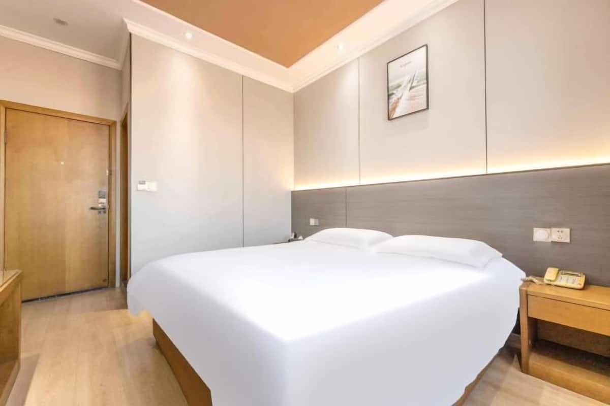 Ein modernes Hotelzimmer mit einem großen Bett, einer Holztür, einem Nachttisch mit Lampe und einem an der Wand befestigten Telefon.