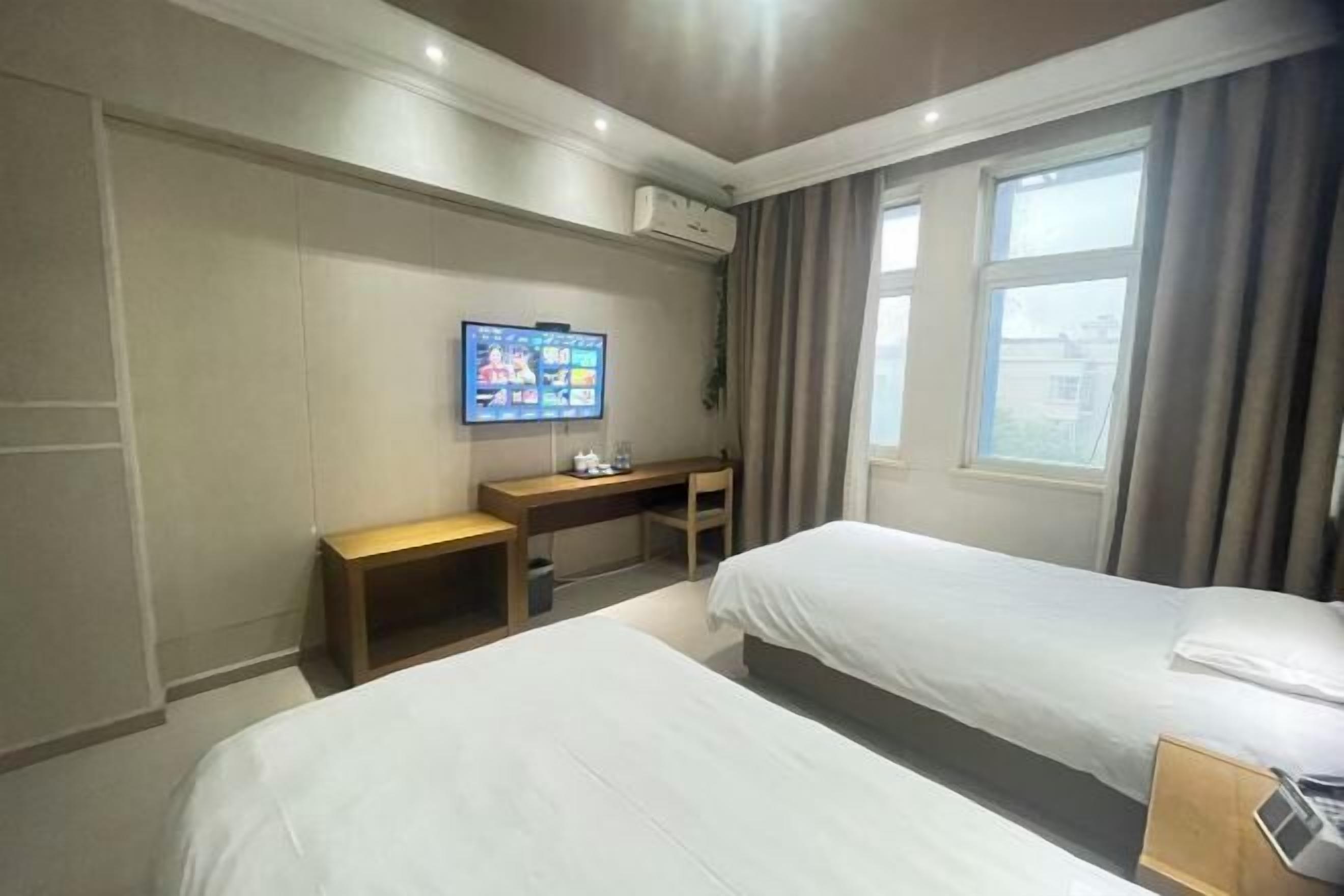 Hotellihuone, jossa on kaksi sänkyä, työpöytä, televisio ja ikkuna, jossa on verhot.