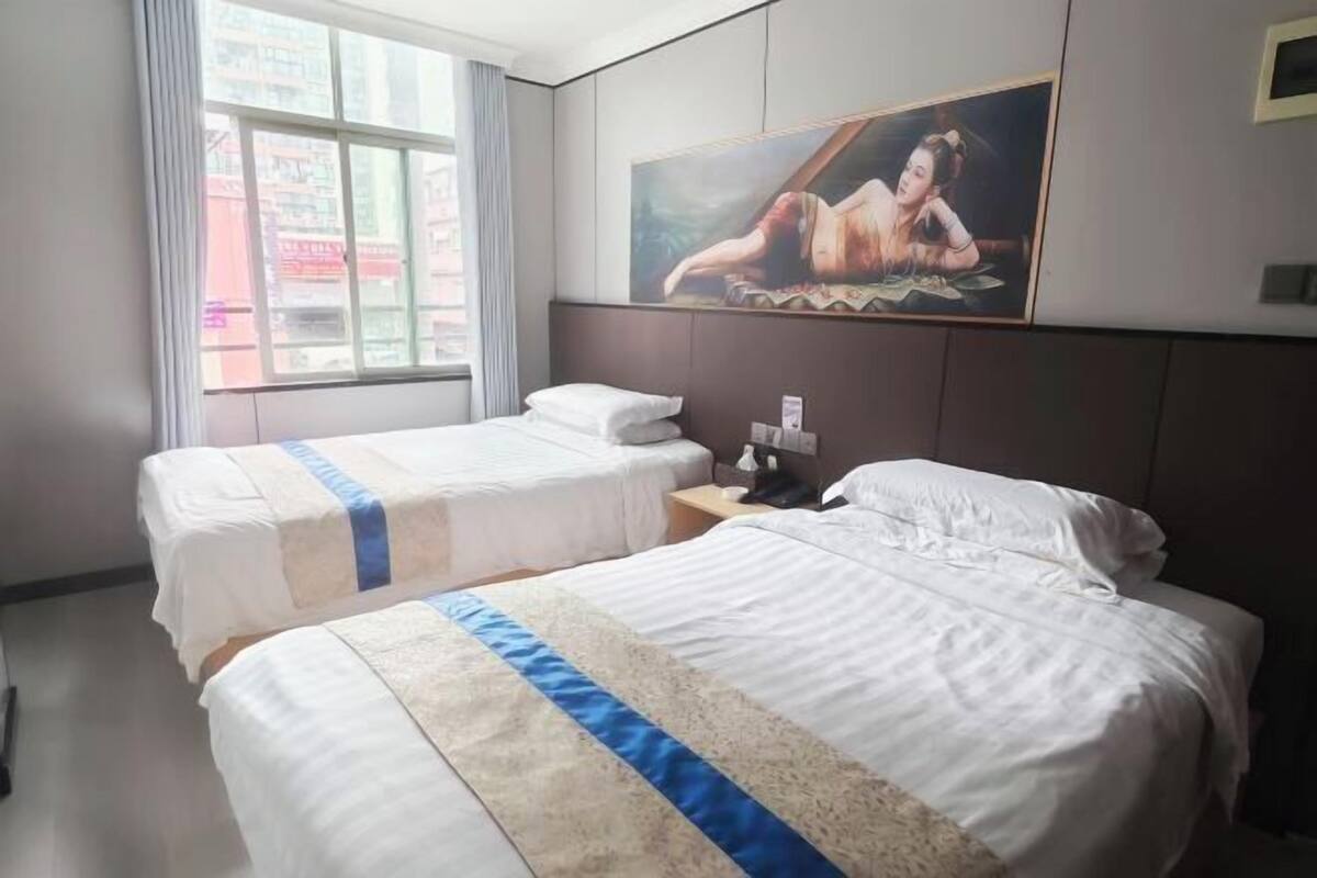 A hotel room with two beds, a large window, and a painting on the wall.