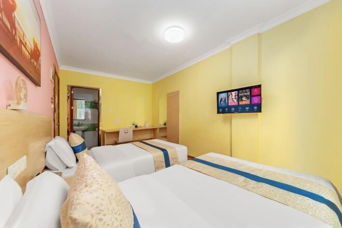 A hotel room with two beds, a TV on the wall, and a desk with a chair.