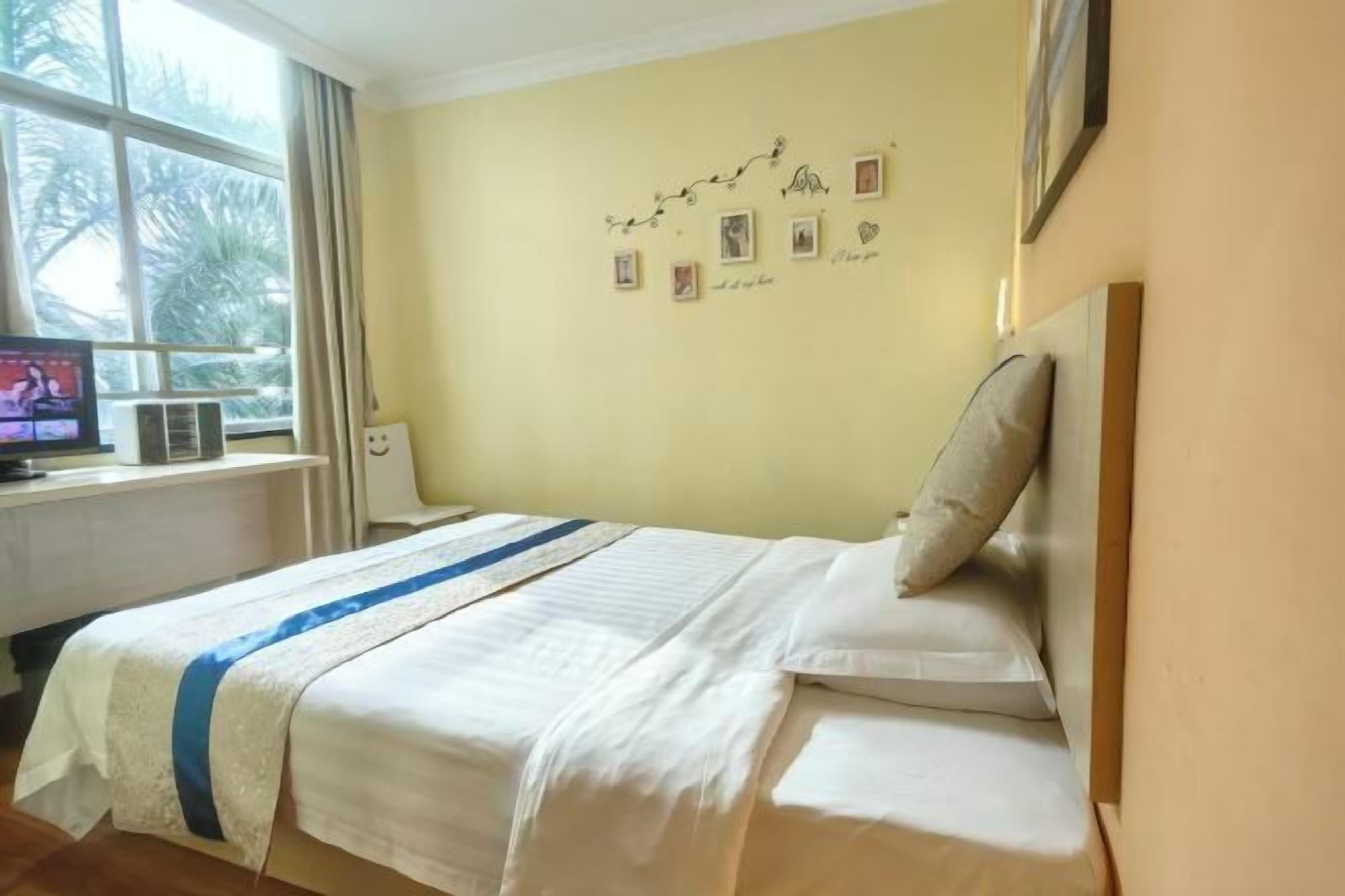 A hotel room with a bed, a window with curtains, a wall with framed pictures, and a television on a desk.
