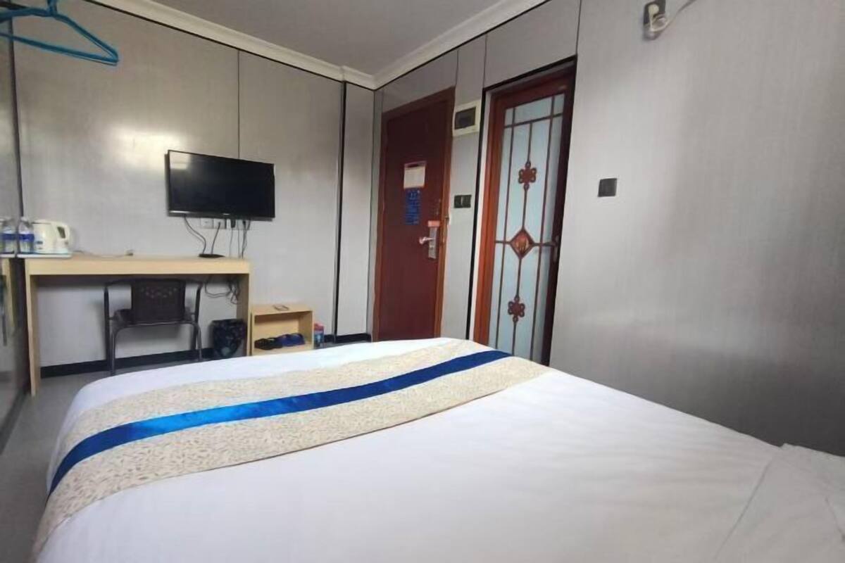 A hotel room with a bed, a desk with a television, a wardrobe, and a door with a decorative handle.