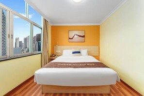 Quarto de hotel com cama, mesa de cabeceira, janela com vista para a cidade e um quadro na parede.