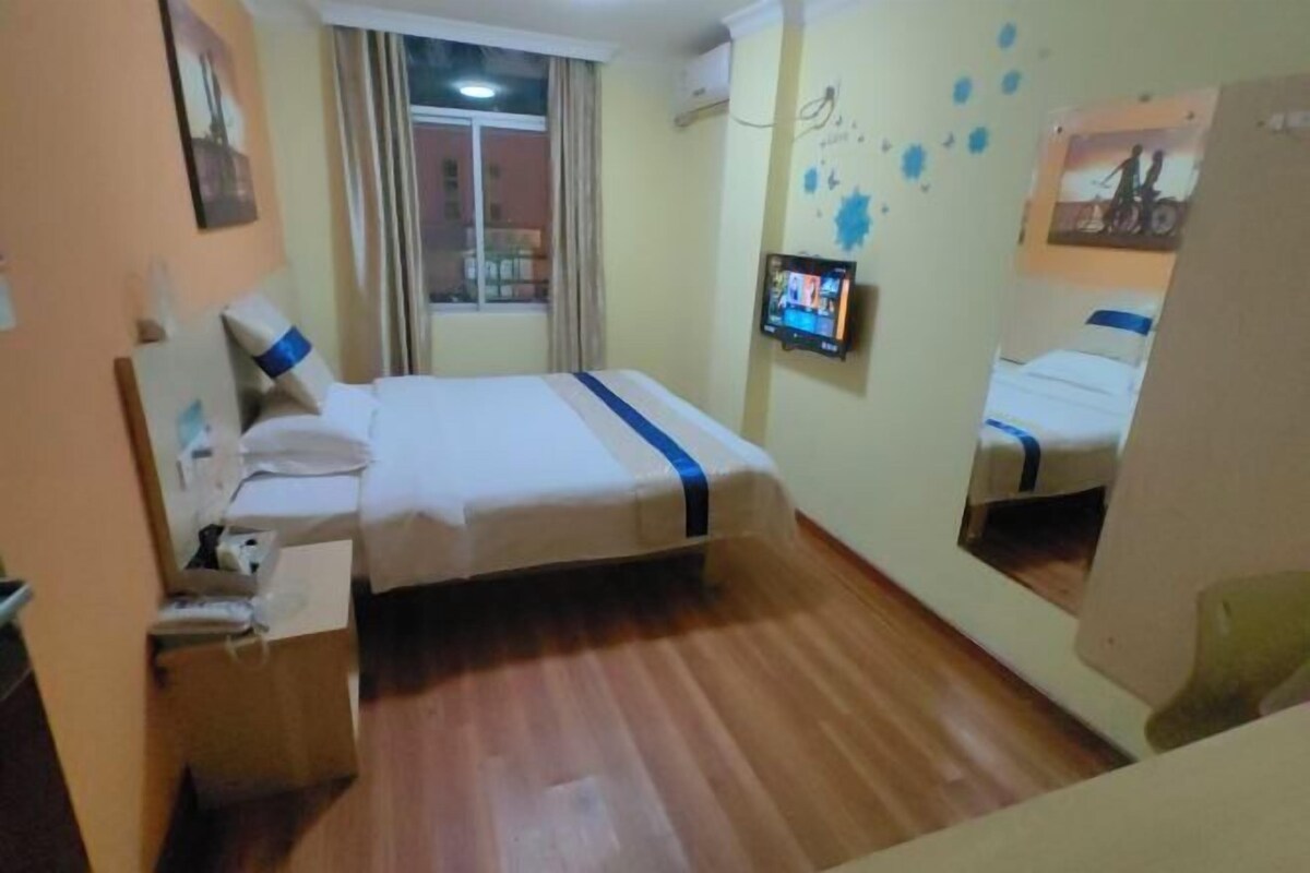 A hotel room with a bed, a TV, a window with curtains, and a mirror.