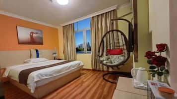 Quarto de hotel com cama, poltrona, cafeteira e janela com cortinas.