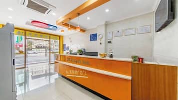 A hotel reception area with a wooden reception desk, a glass door entrance, and a wall-mounted television.