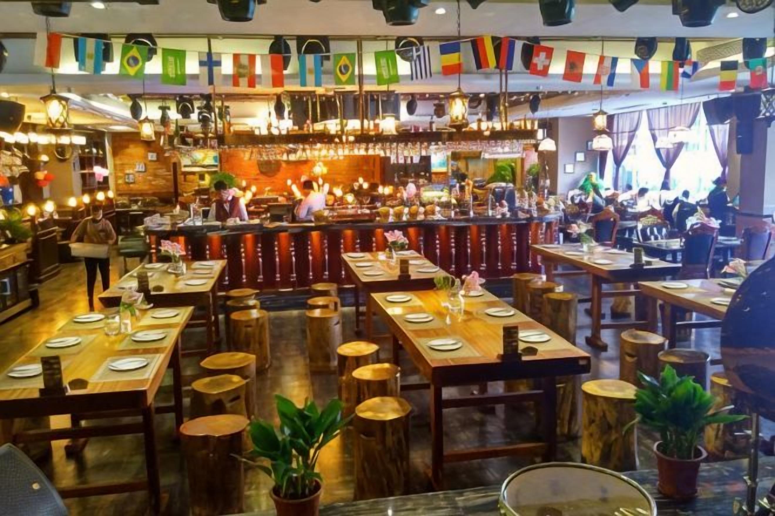 Un restaurante con varias mesas y sillas, una zona de bar y decoraciones colgantes.