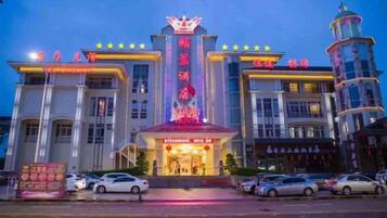 A multi-story building with a prominent entrance, a tower with a spire, and a series of lights along the facade.