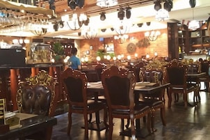 Interior de un restaurante con varias mesas y sillas, una zona de bar con vasos y botellas, y una persona al fondo.