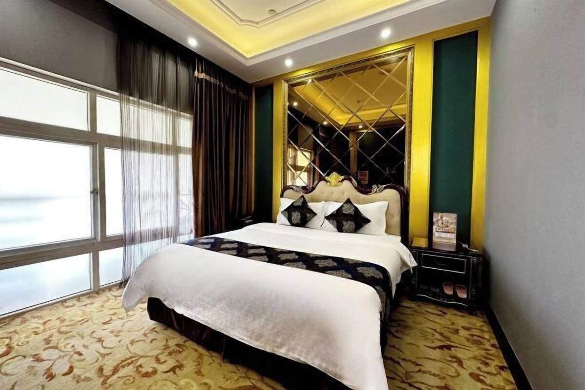 Ein Hotelzimmer mit einem großen Bett, einem Nachttisch, einem Spiegel und einem Fenster mit Vorhängen.