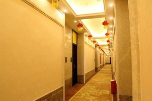 Un pasillo con alfombra estampada, puertas y decoraciones rojas colgantes.