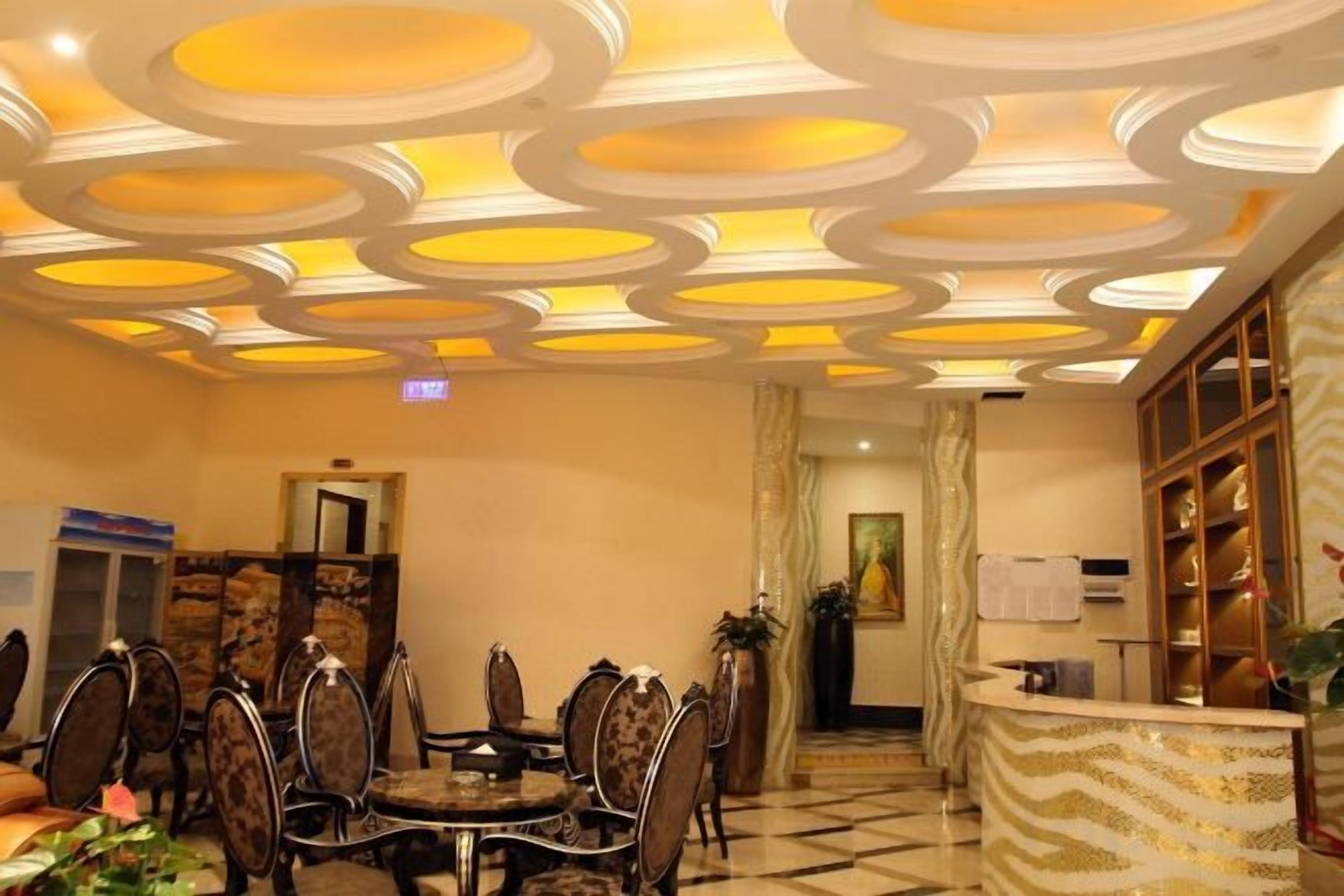 A hotel lobby with a round dining table, chairs, a reception desk, and a patterned ceiling.