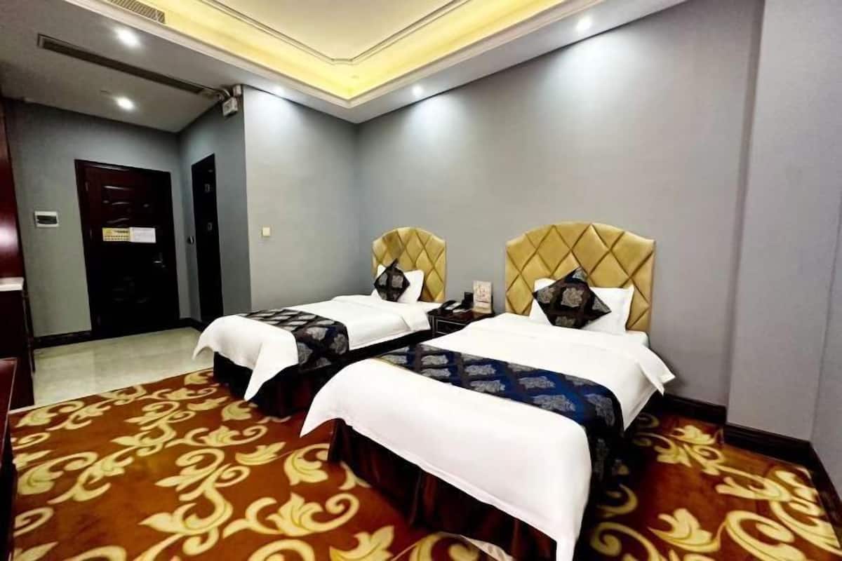 Ein Hotelzimmer mit zwei Betten, Teppichboden und einer Tür im Hintergrund.