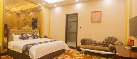 A hotel room with a large bed, a sofa, a small table, and a TV.