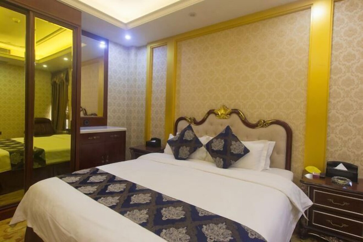 A hotel room with a large bed, a nightstand, a mirror, and a wardrobe.