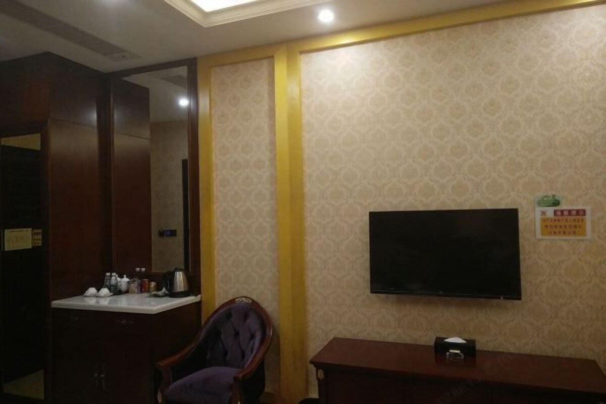 A hotel room with a wooden desk, a chair, a television mounted on the wall, and a small table with a remote control.