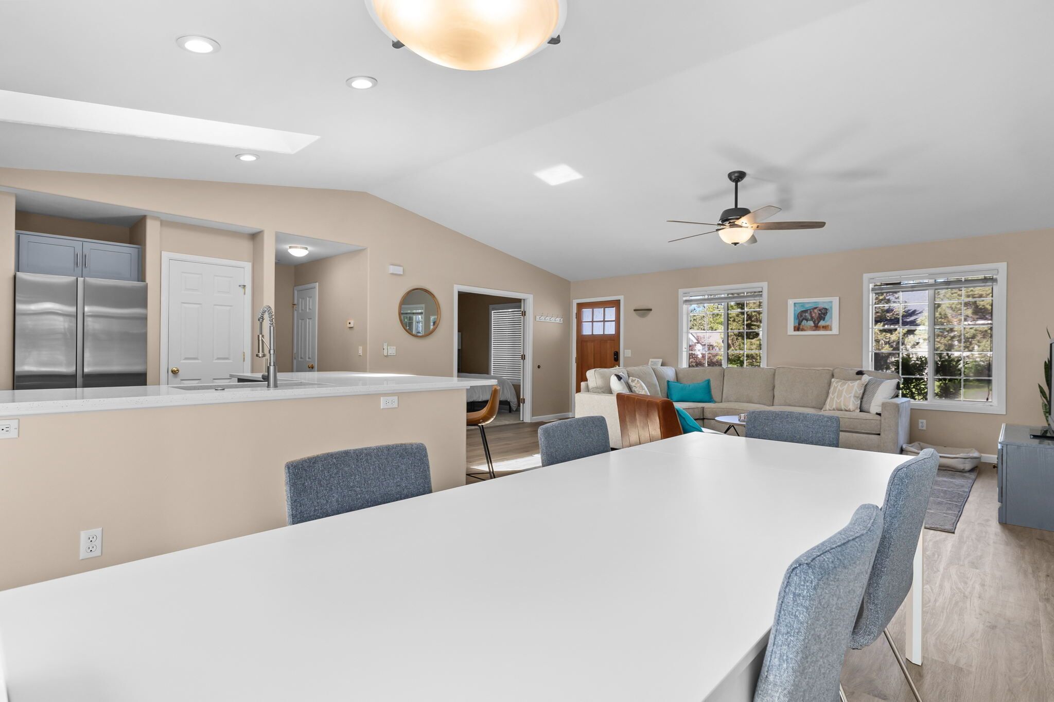 A modern kitchen with built-in appliances, a dining area with a large table and chairs, and a living room with a sofa and a ceiling fan.