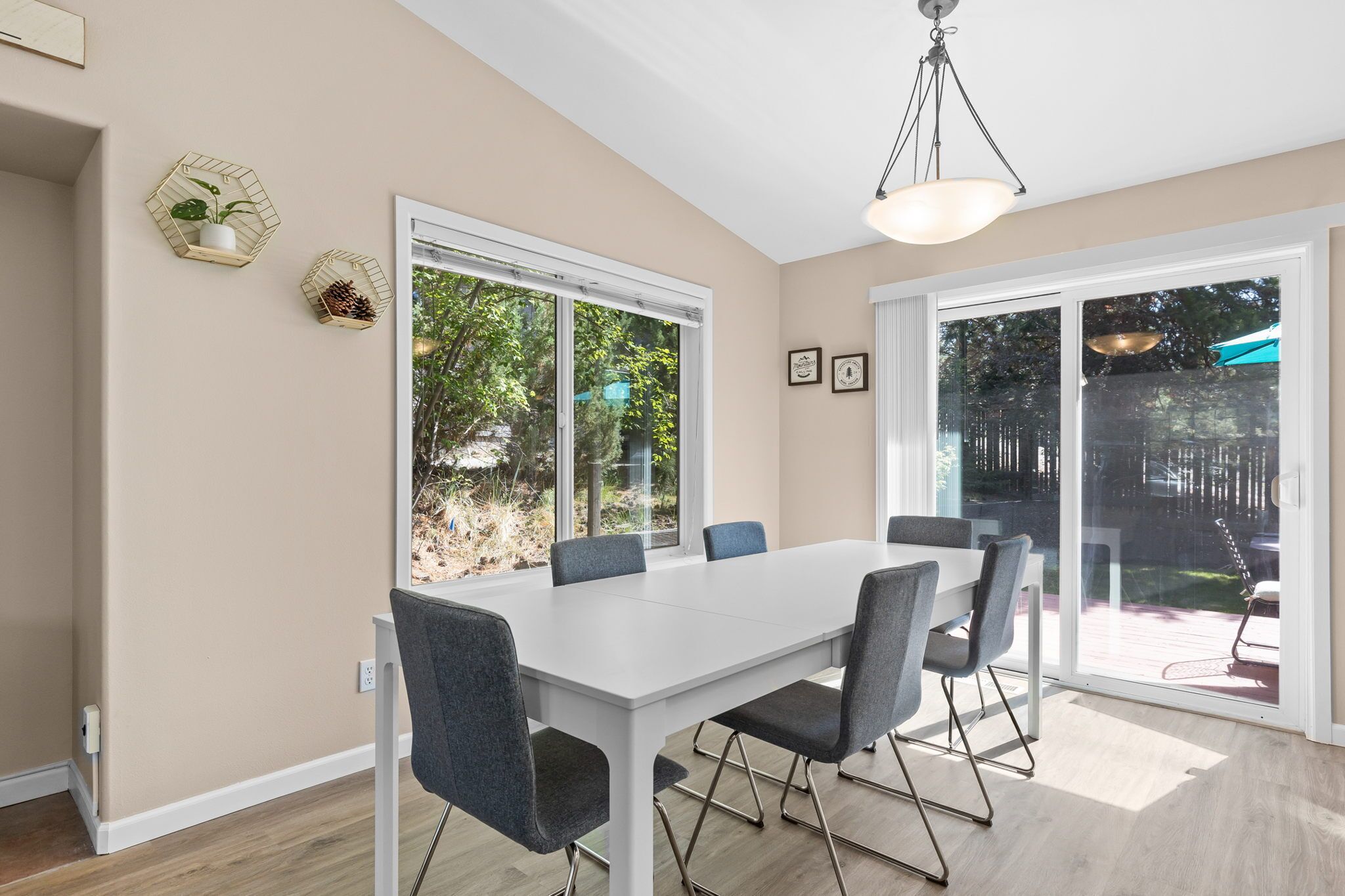 Uma sala de jantar moderna com mesa branca e cadeiras cinzentas, janelas amplas e vista para o exterior.