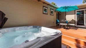 Un jacuzzi en una terraza de madera con una mesa y sillas, y un área de patio techada.
