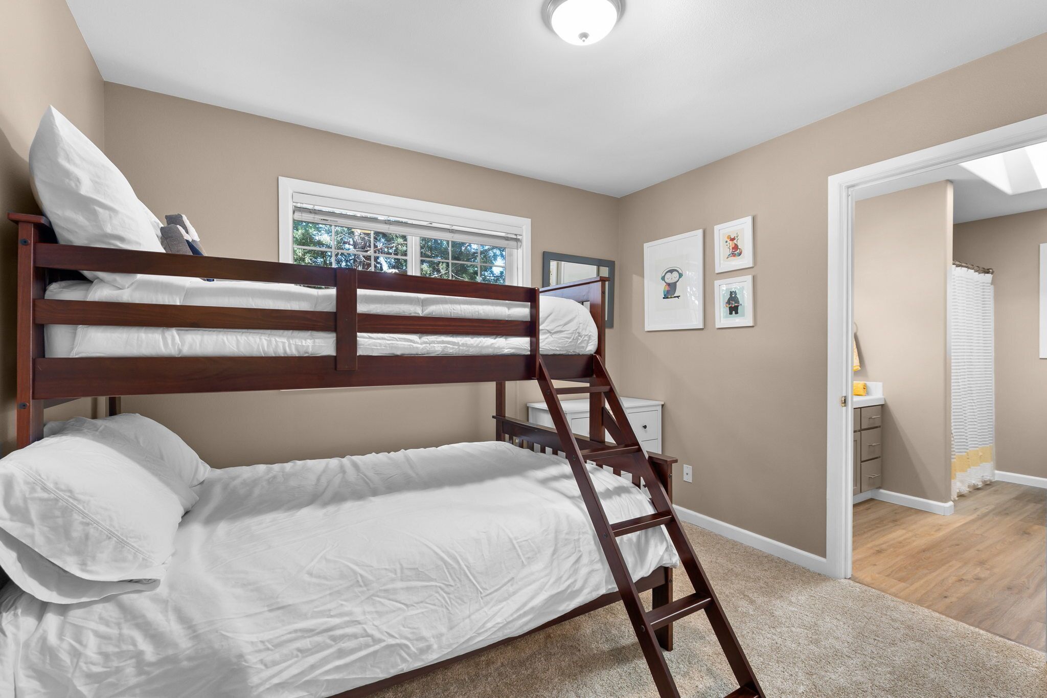 Une chambre avec un lit superposé, une échelle, une fenêtre et une porte donnant sur une autre pièce.