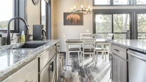 A modern kitchen with granite countertops, stainless steel appliances, and a dining area with a white table and chairs. - Wernski Lodge – Stunning Views, Hot Tub & Spacious Retreat (Lead)
