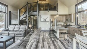 A spacious living area with a large sofa, a dining area with bar stools, a kitchen with modern appliances, and a staircase leading to an upper level. - Wernski Lodge – Stunning Views, Hot Tub & Spacious Retreat (Lead)