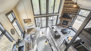 A spacious living area with a fireplace, large windows, and a high ceiling. - Wernski Lodge – Stunning Views, Hot Tub & Spacious Retreat (Lead)