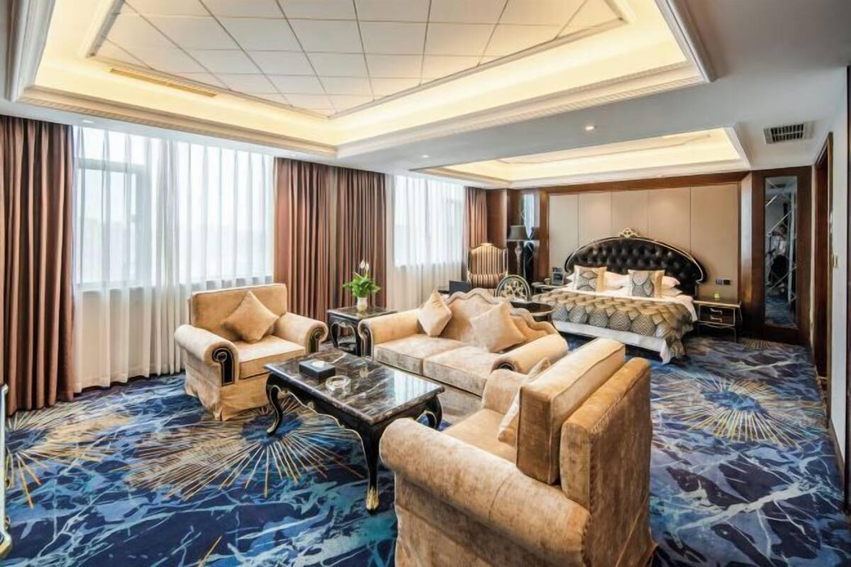 A hotel room with a large bed, two sofas, a coffee table, and a carpeted floor.