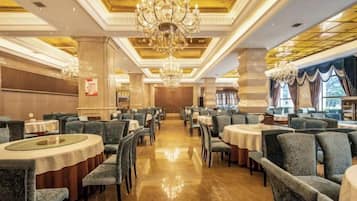A spacious dining area with round tables and chairs, chandeliers, and a polished floor.