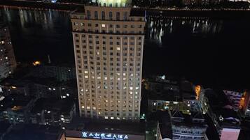 Un hotel moderno de gran altura con varios pisos, una cúpula destacada en la parte superior y vista al río de noche.