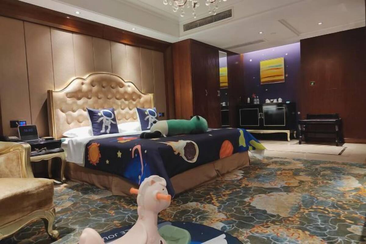 A hotel room with a large bed, a desk with a computer, a plush chair, and a decorative rug.