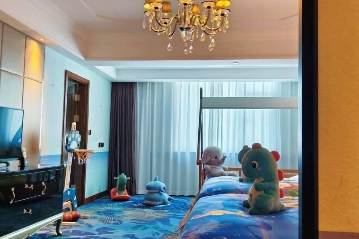 A hotel room with a bed, a TV, a chandelier, and plush toys.