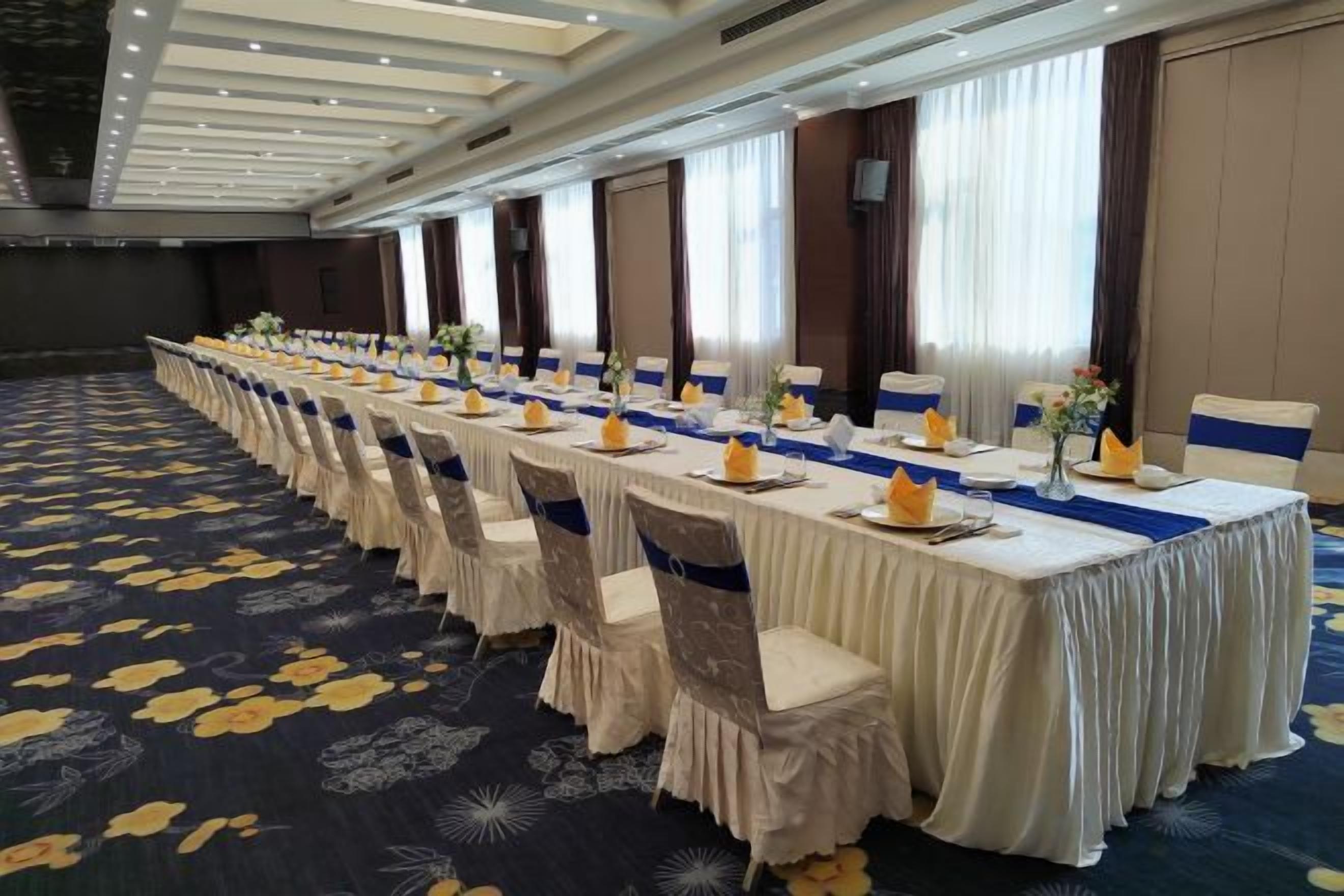 A long banquet table set with chairs, centerpieces, and a blue runner.