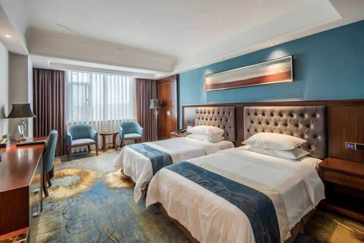 A hotel room with two beds, a desk, a chair, a small table, and a window with curtains.