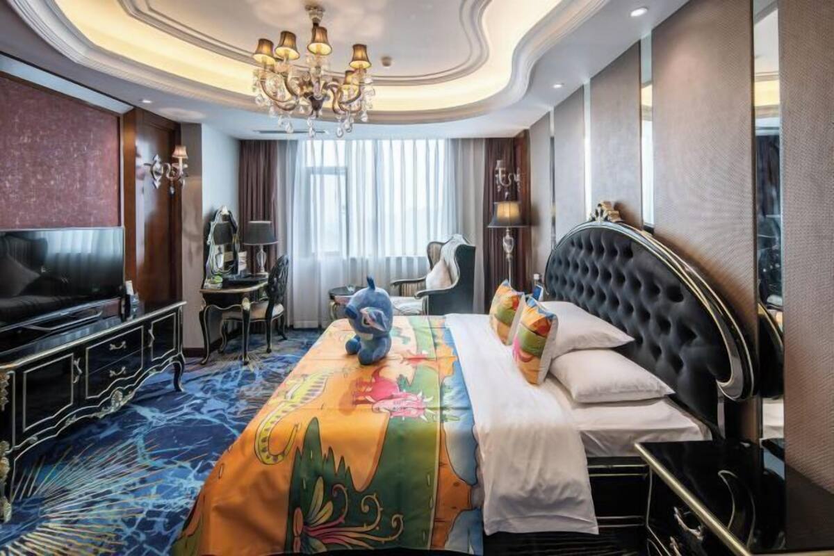 A hotel room with a large bed, a TV, a desk, and a chandelier.