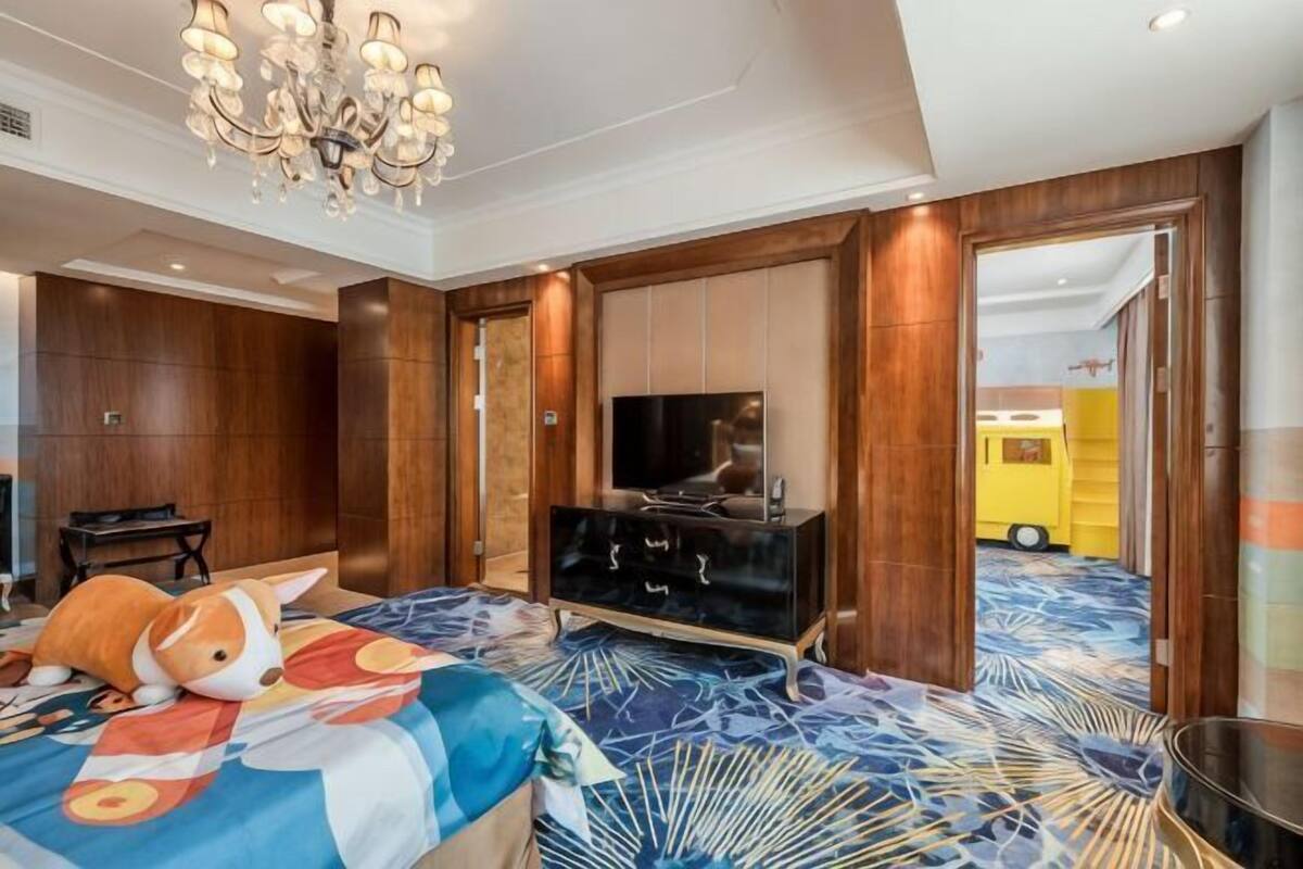 A hotel room with a bed, a television, a wooden wardrobe, and a chandelier.