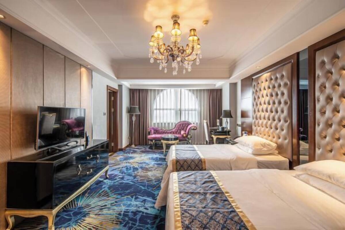 A hotel room with a large bed, a television, a seating area with a chair, and a decorative chandelier.