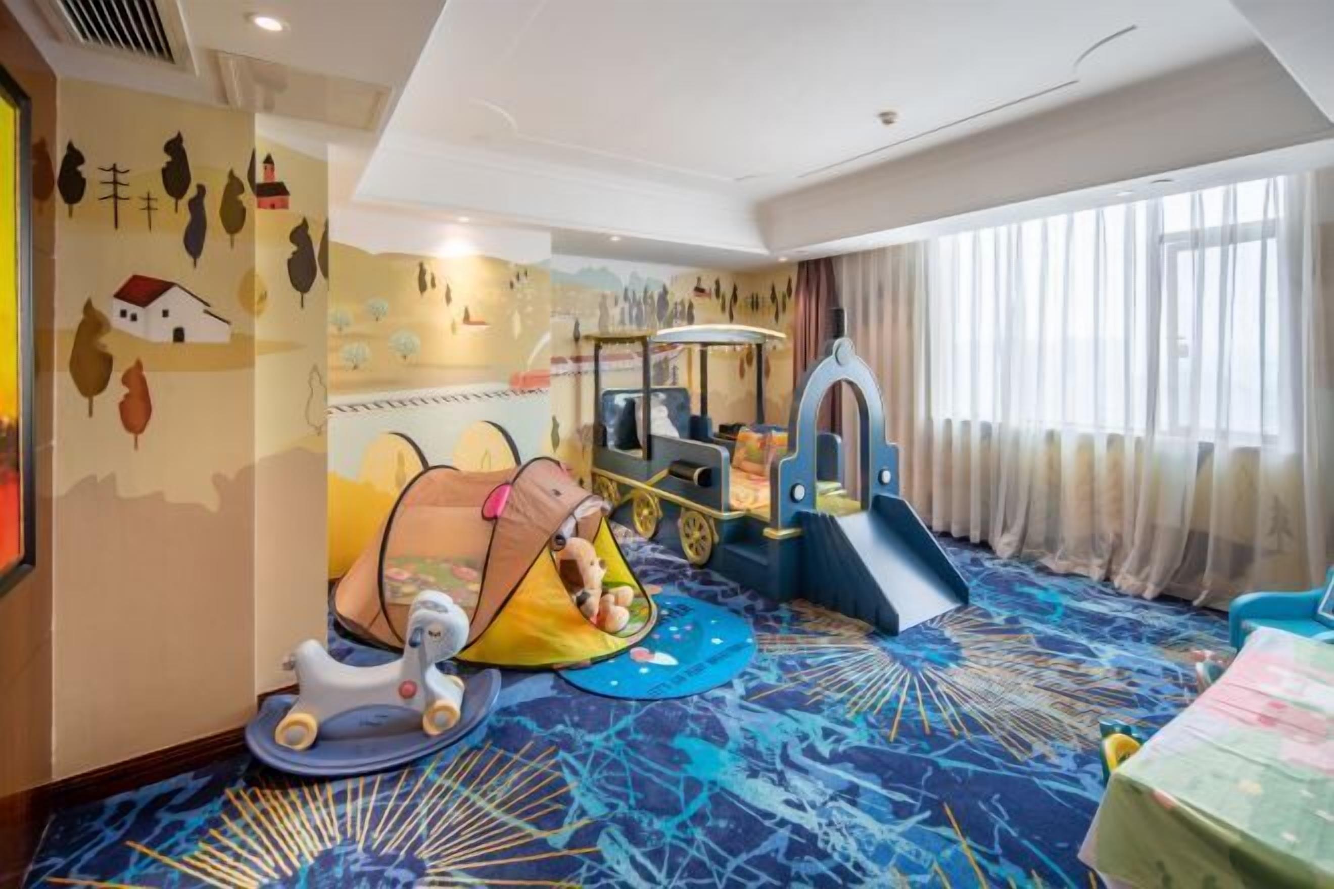 Zona infantil con un juguete para montar, una carpa pequeña y un parque de juegos.
