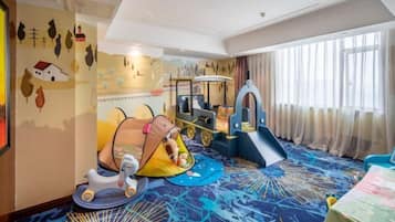 Zona infantil con un juguete para montar, una carpa pequeña y un parque de juegos.