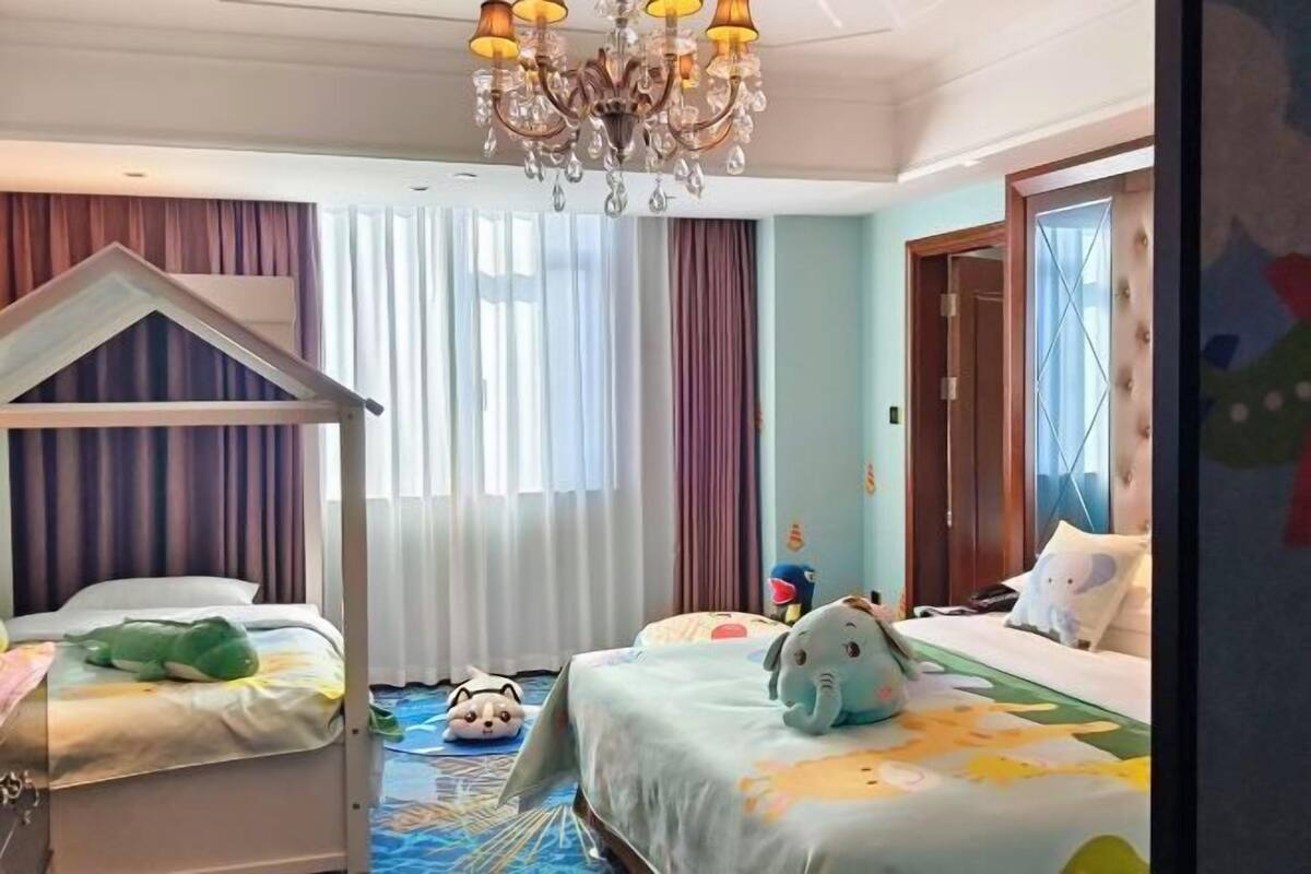 A hotel room with a bunk bed, a chandelier, a play area with plush toys, and a large window with curtains.