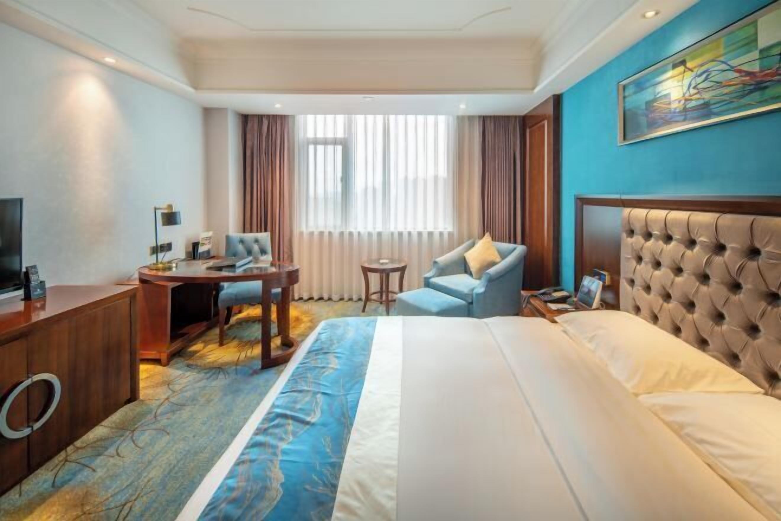 A hotel room with a large bed, a desk, a chair, a television, and a window with curtains.