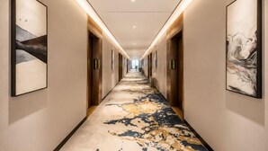 A hotel hallway with a patterned carpet, framed artwork on the walls, and a long corridor. - Jinxiu Xiangjiang Hotel (Foshan Jinsha) (Foshan)