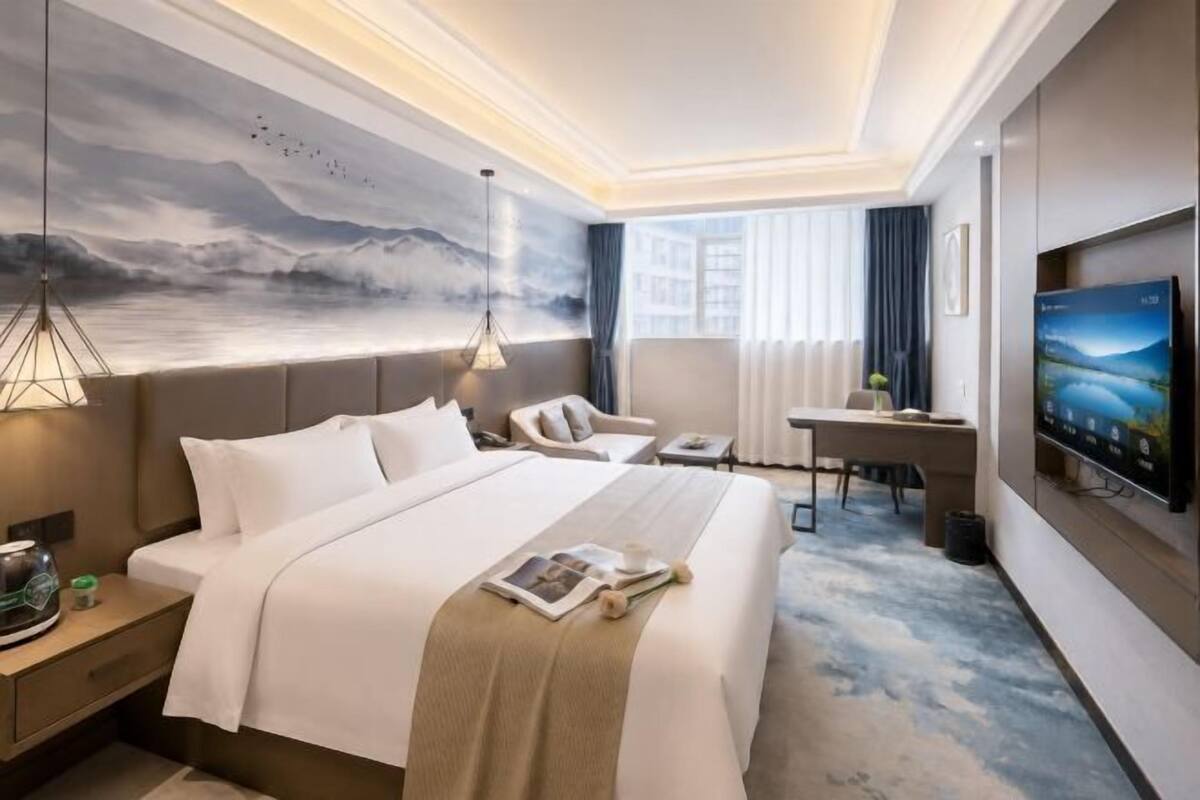 Une chambre d’hôtel avec un grand lit, un bureau, une chaise, une télévision et un tableau au mur.