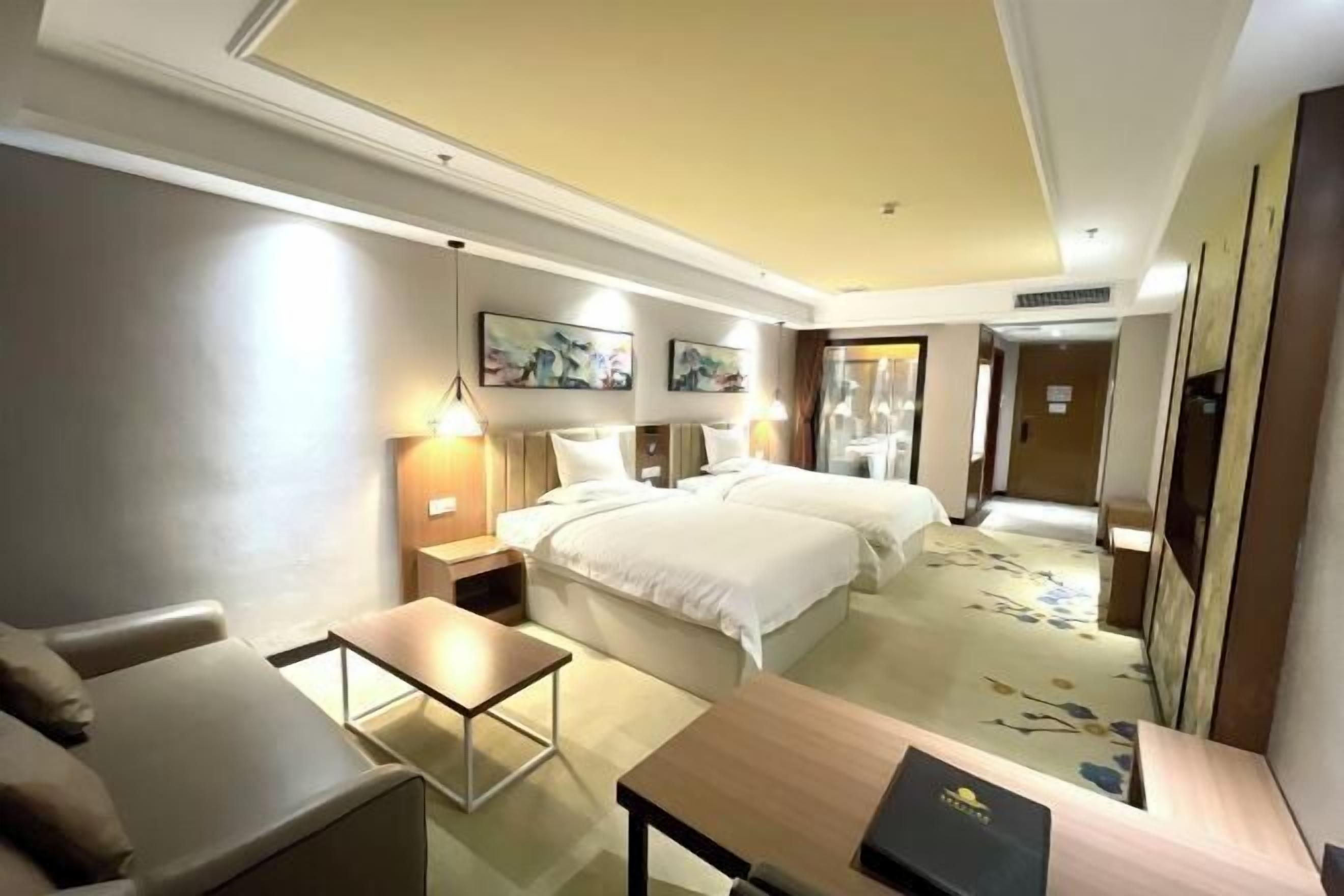 A hotel room with a bed, a desk, a chair, a nightstand, and a wall-mounted lamp.